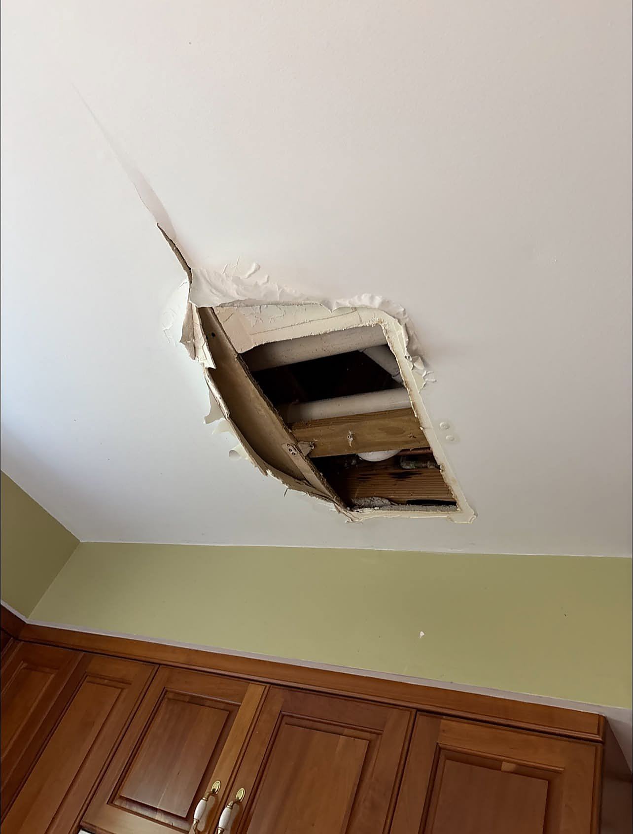 Hole cut in a ceiling exposing PVC drain pipes and wet framing below a bathroom
