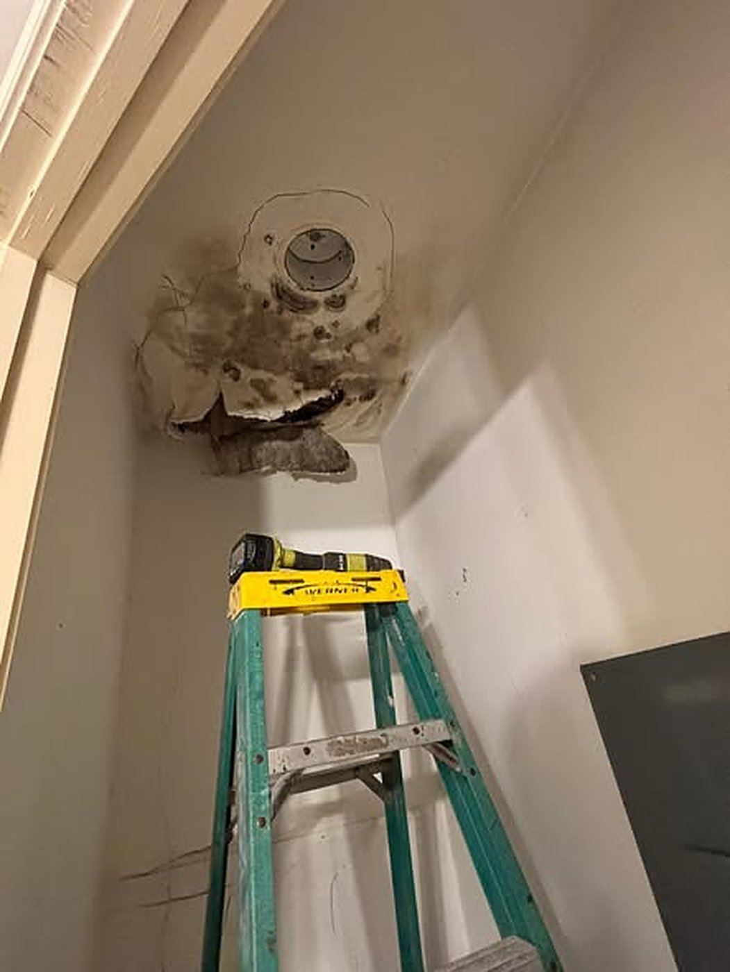 Water-damaged ceiling with dark staining around an air conditioning vent in a closet