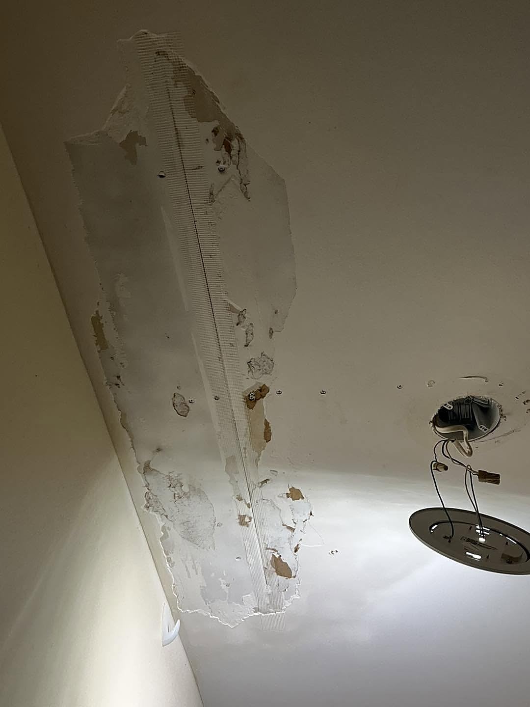 Ceiling drywall peeling away with mesh tape exposed and a light fixture removed