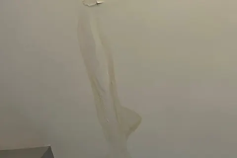 Long yellow-brown water stain streak with peeling paint on a white ceiling