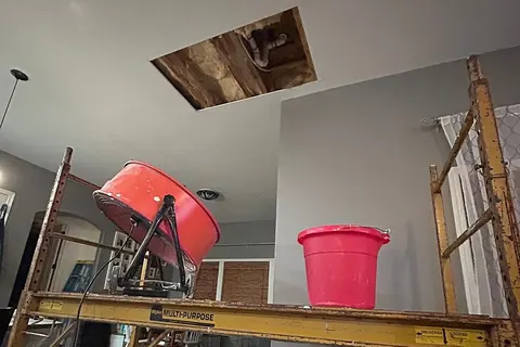 Scaffold holding a fan and bucket below an opened ceiling for drying and water removal